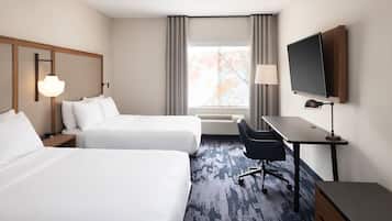Habitación de hotel con dos camas, un escritorio, una silla, un televisor y una ventana con cortinas.