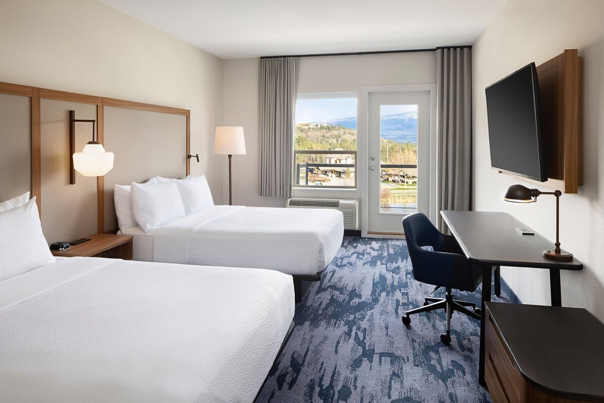 Ein Hotelzimmer mit zwei Betten, einem Schreibtisch, einem Sessel, einem Fernseher und Blick ins Freie.