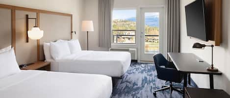 Ein Hotelzimmer mit zwei Betten, einem Schreibtisch, einem Sessel, einem Fernseher und Blick ins Freie.
