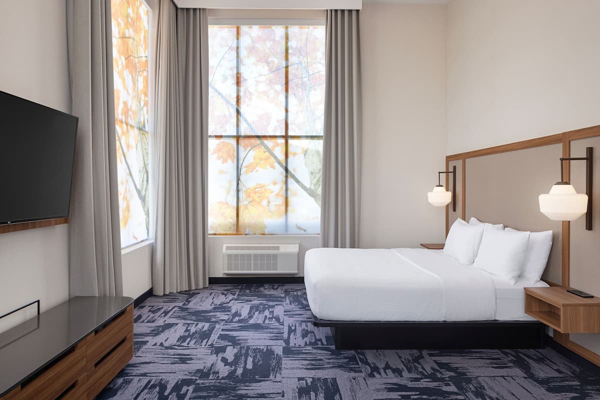 A modern hotel room with a large bed, a flat-screen TV, and a large window with curtains.