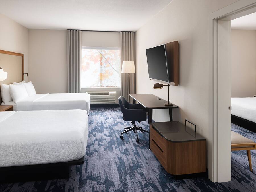 Habitación de hotel con dos camas, un escritorio, un televisor y una ventana con cortinas.