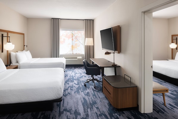 A hotel room with two beds, a desk, a TV, and a window with curtains.