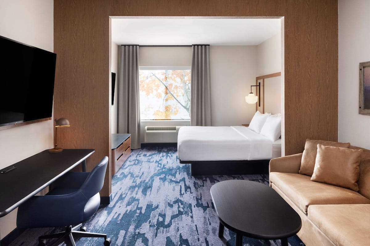 A hotel room with a bed, a desk with a chair, a sofa, a TV, and a window with curtains.