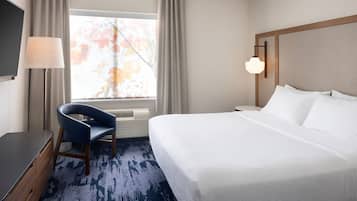 Une chambre d’hôtel avec un lit, un bureau, une chaise, une lampe et une fenêtre avec des rideaux.