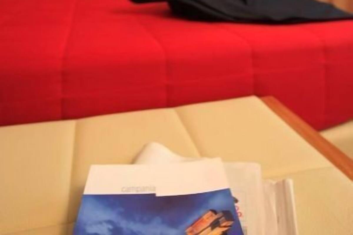 A hotel room with a red bedspread, a framed picture on the wall, and a nightstand with a lamp.