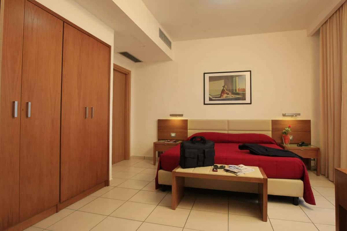 A hotel room with a large bed, wooden wardrobe, bedside tables, and a painting on the wall.