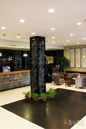 A reception area with a black decorative pillar, potted plants, and a reception desk. - Beijing Tiantan Xingcheng Hotel (Beijing)