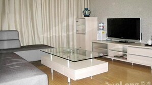 Ett modernt vardagsrum med en grå soffa, ett soffbord i glas, en platt-TV och ett vitt skåp.