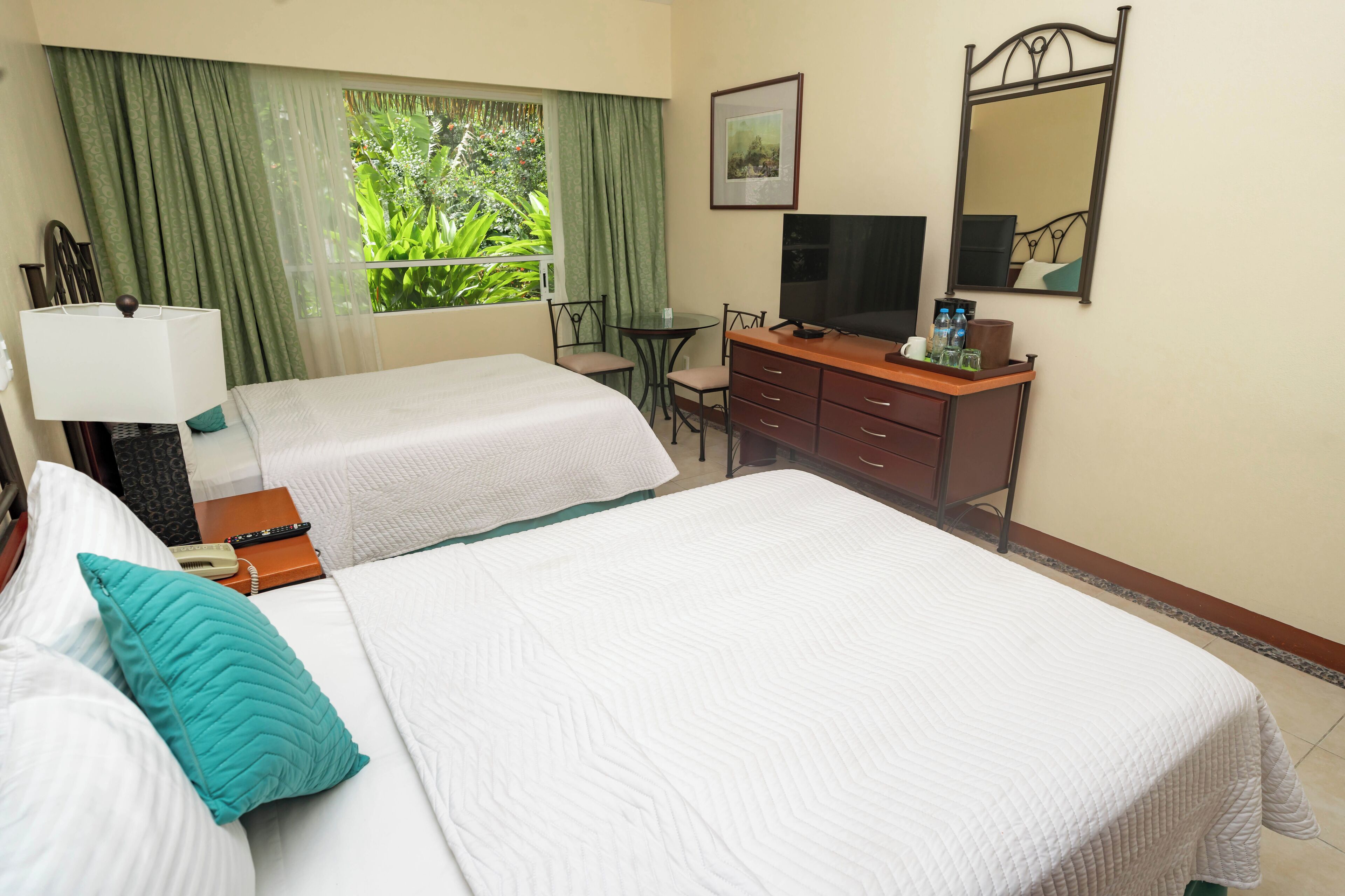 A hotel room with two beds, a desk with a TV, a mirror, and a window with curtains.