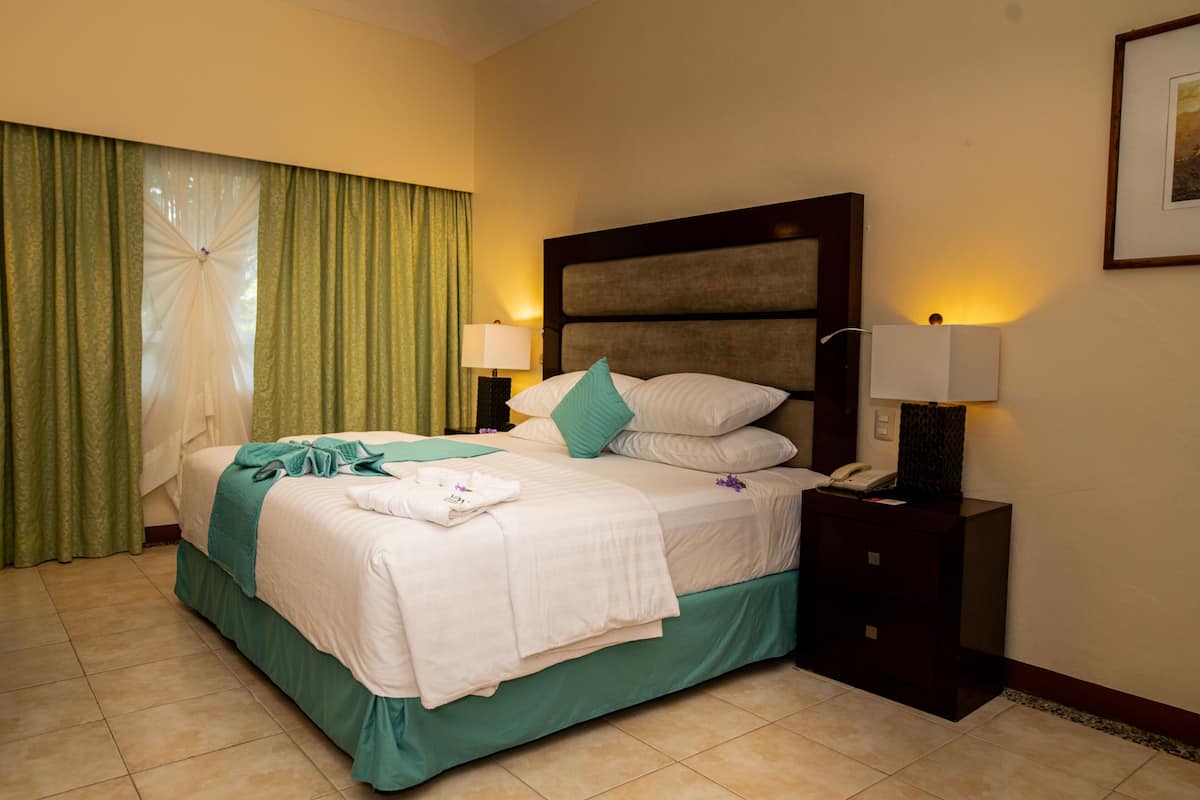 Ein Hotelzimmer mit Bett, Nachttisch, Lampe, Telefon und Vorhang.