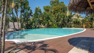 A swimming pool with a curved edge, surrounded by palm trees and a thatched-roof structure.