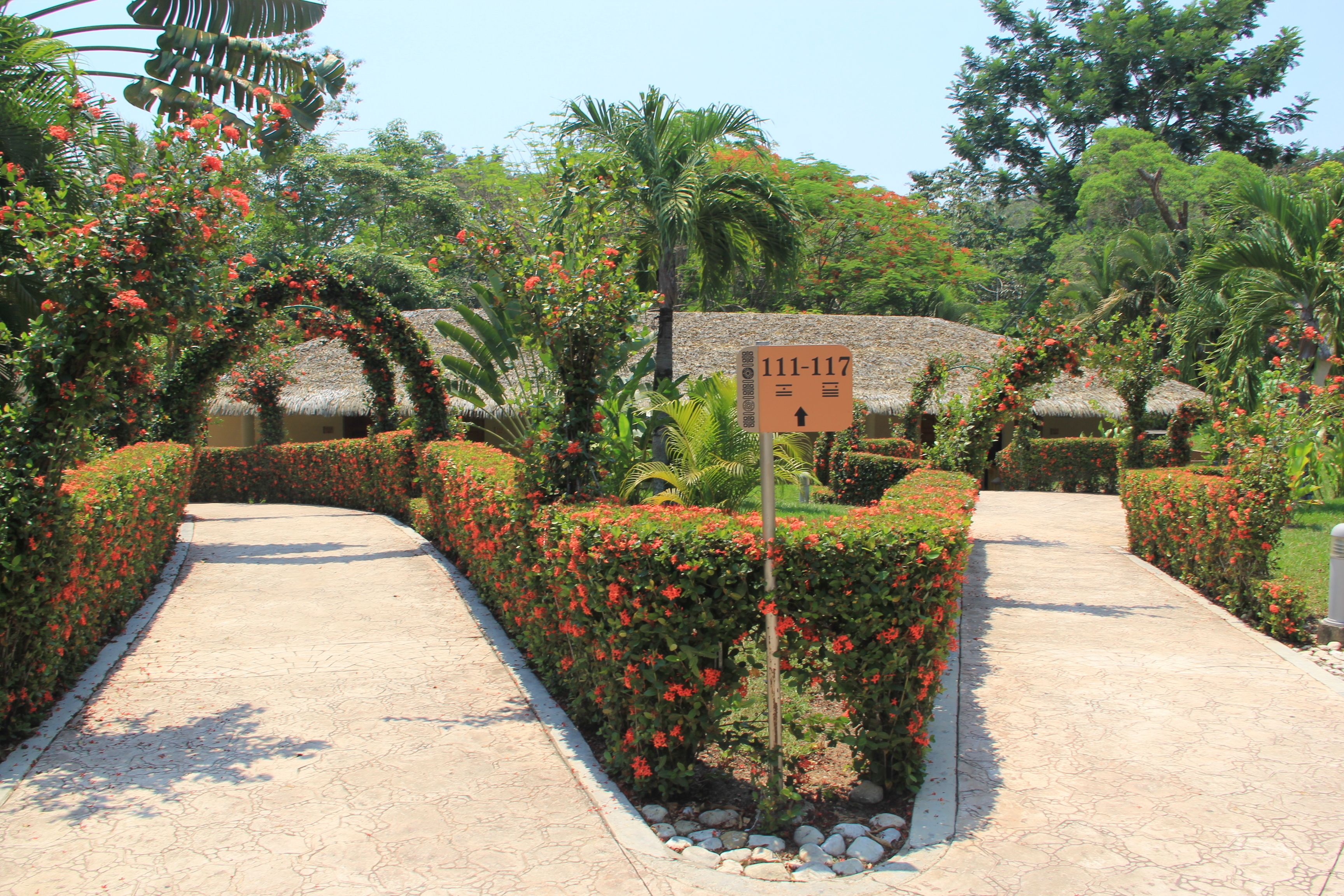 A pathway lined with red flowers and a sign indicating room numbers 111-117.