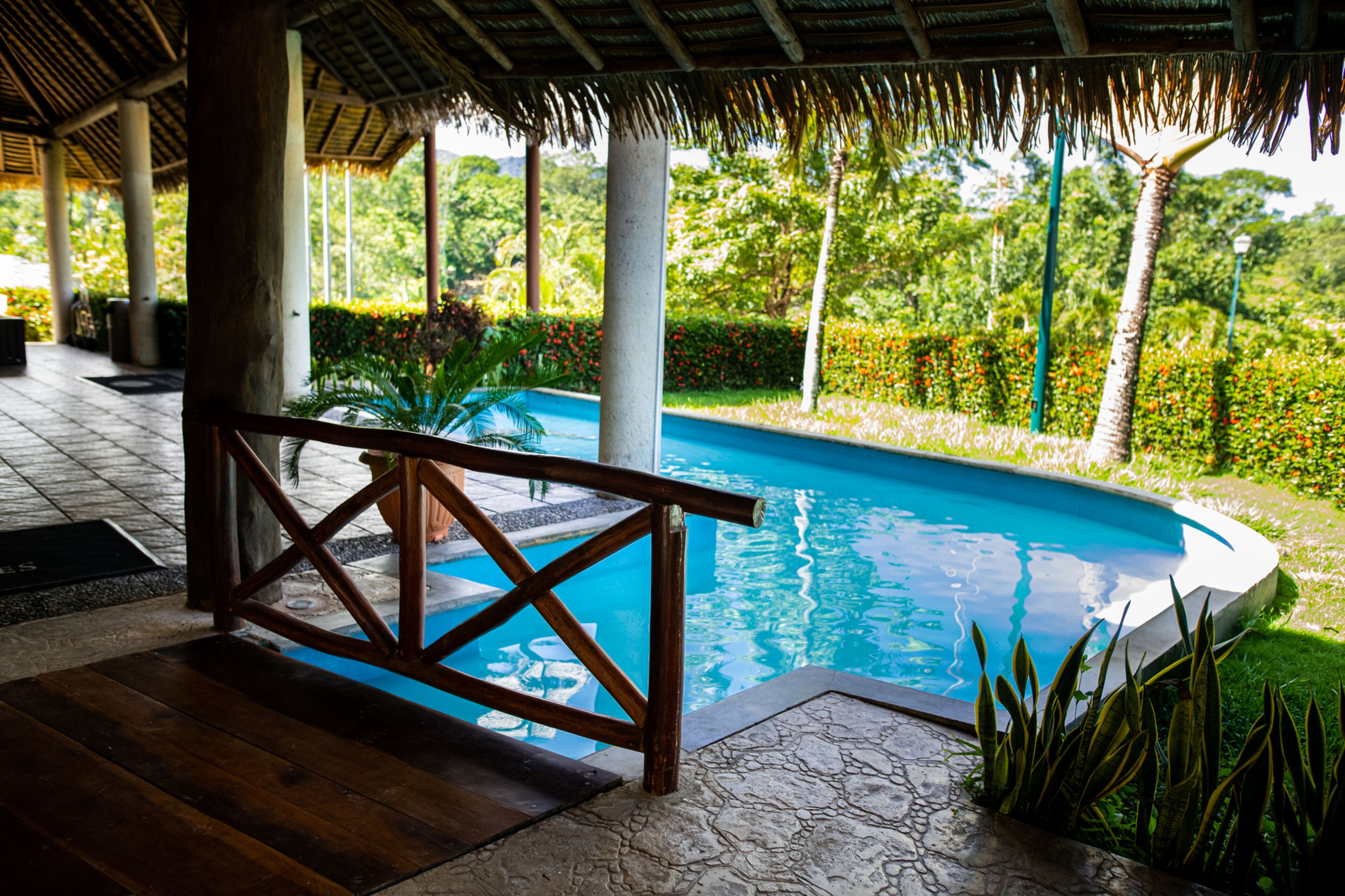A pool area with a wooden deck and a thatched roof structure.