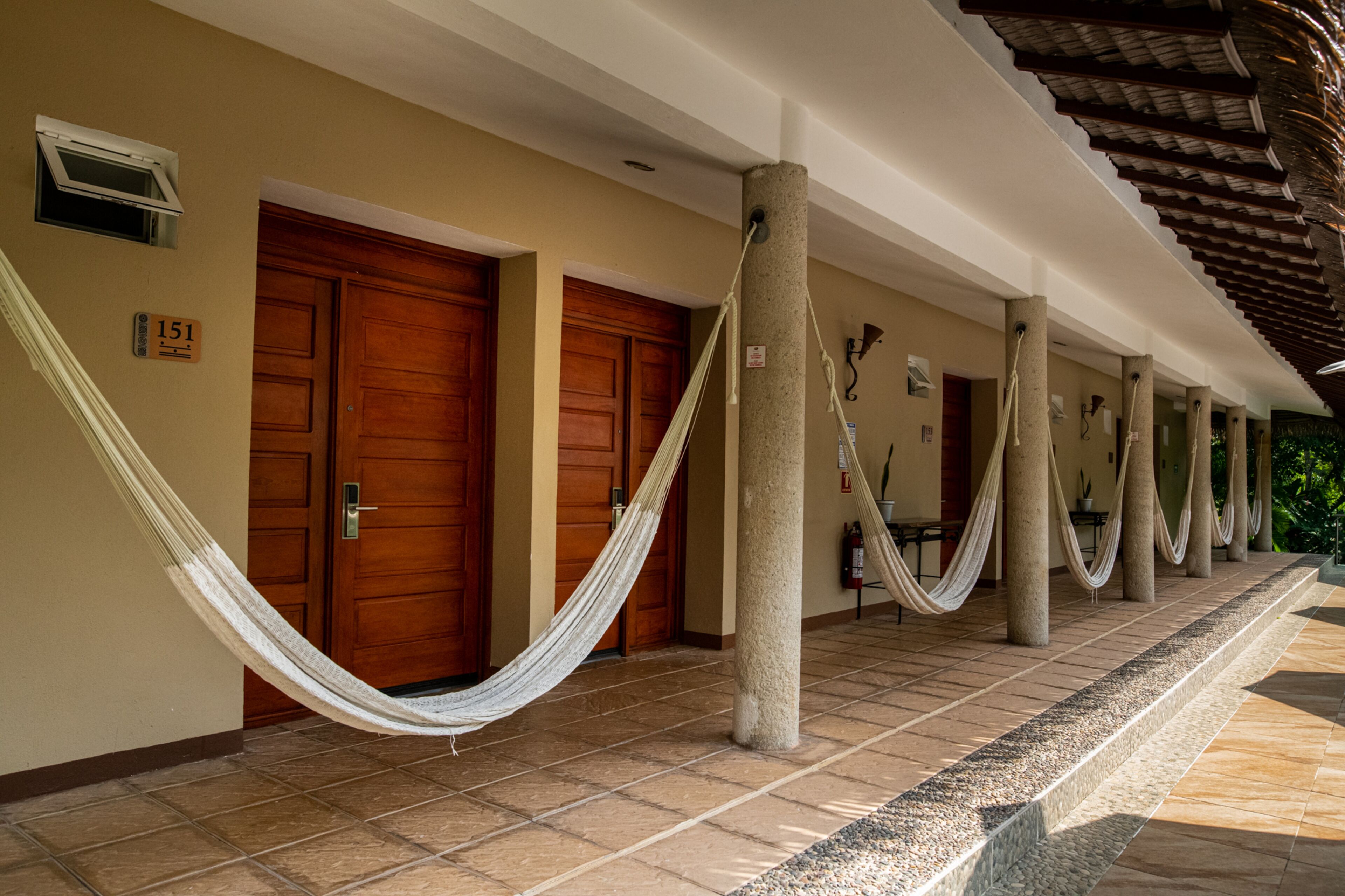 A hotel corridor with wooden doors, a hammock, and columns.