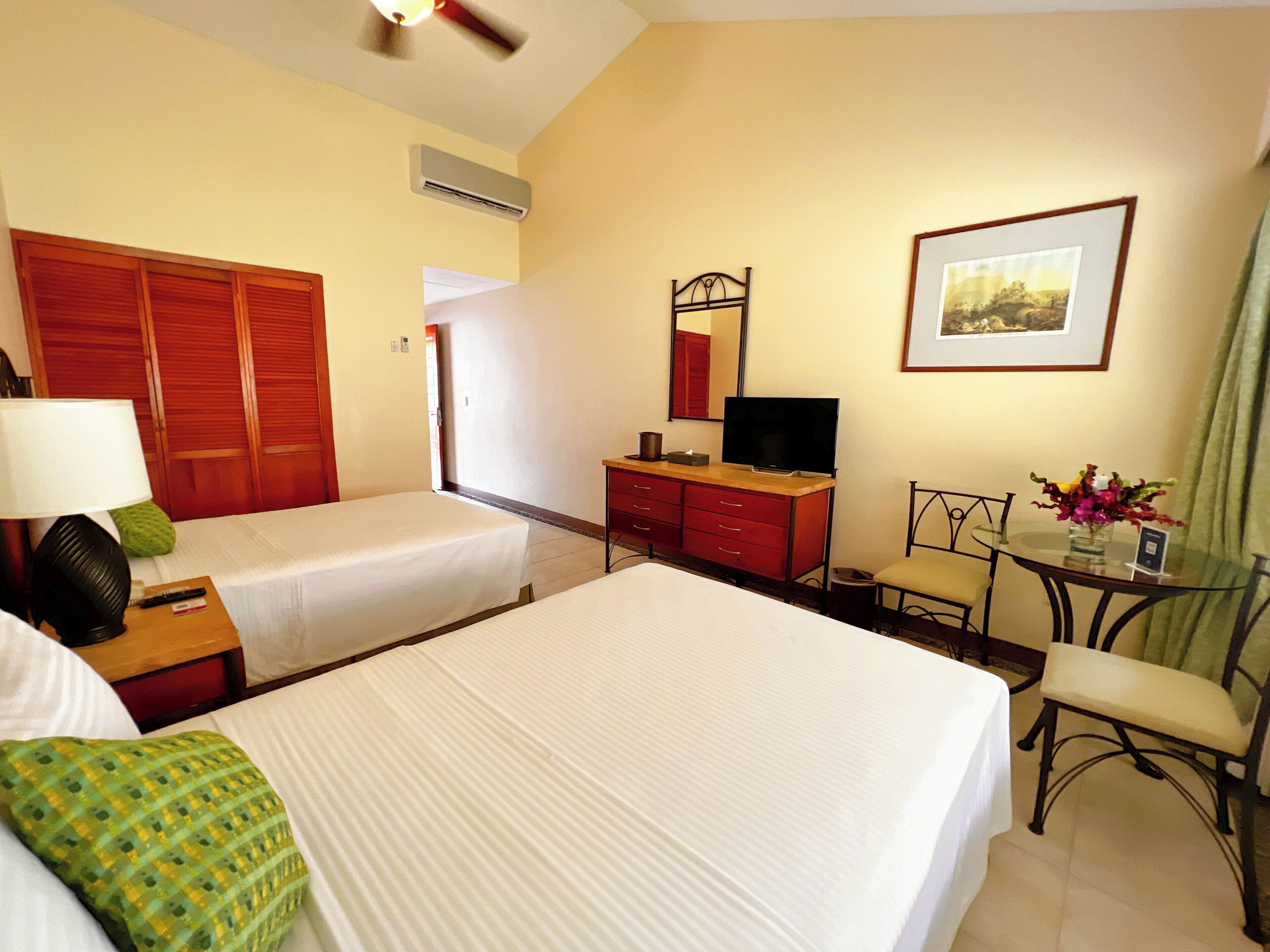 A hotel room with two beds, a desk with a chair, a television, a mirror, and a framed picture on the wall.