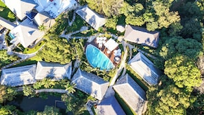 Vue aérienne d’un complexe hôtelier comprenant plusieurs bâtiments, une piscine et une végétation luxuriante.