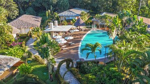 A resort with a swimming pool, lounge chairs, and thatched-roof buildings surrounded by lush greenery. - Hotel Villa Mercedes Palenque (Palenque)