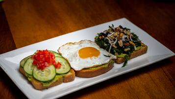 A white rectangular plate with three different food items: a fried egg, a sandwich with cucumber slices, and a salad with nuts.