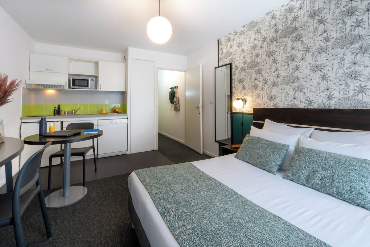 Habitación de hotel con cama, escritorio, silla, microondas y una pequeña cocina.