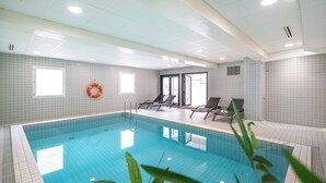 An indoor swimming pool with clear blue water, tiled walls, and a lifebuoy on the wall.