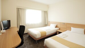 Una habitación de hotel con dos camas, un escritorio con televisor y una ventana con cortinas.