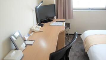 Habitación de hotel con escritorio, computadora, teléfono, lámpara, cama y ventana con cortinas.