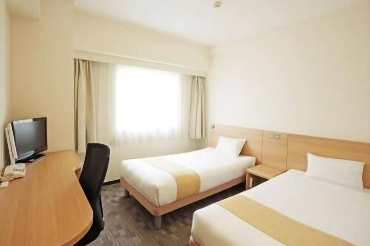 Habitación de hotel con cama, escritorio, silla, televisor y ventana con cortinas.
