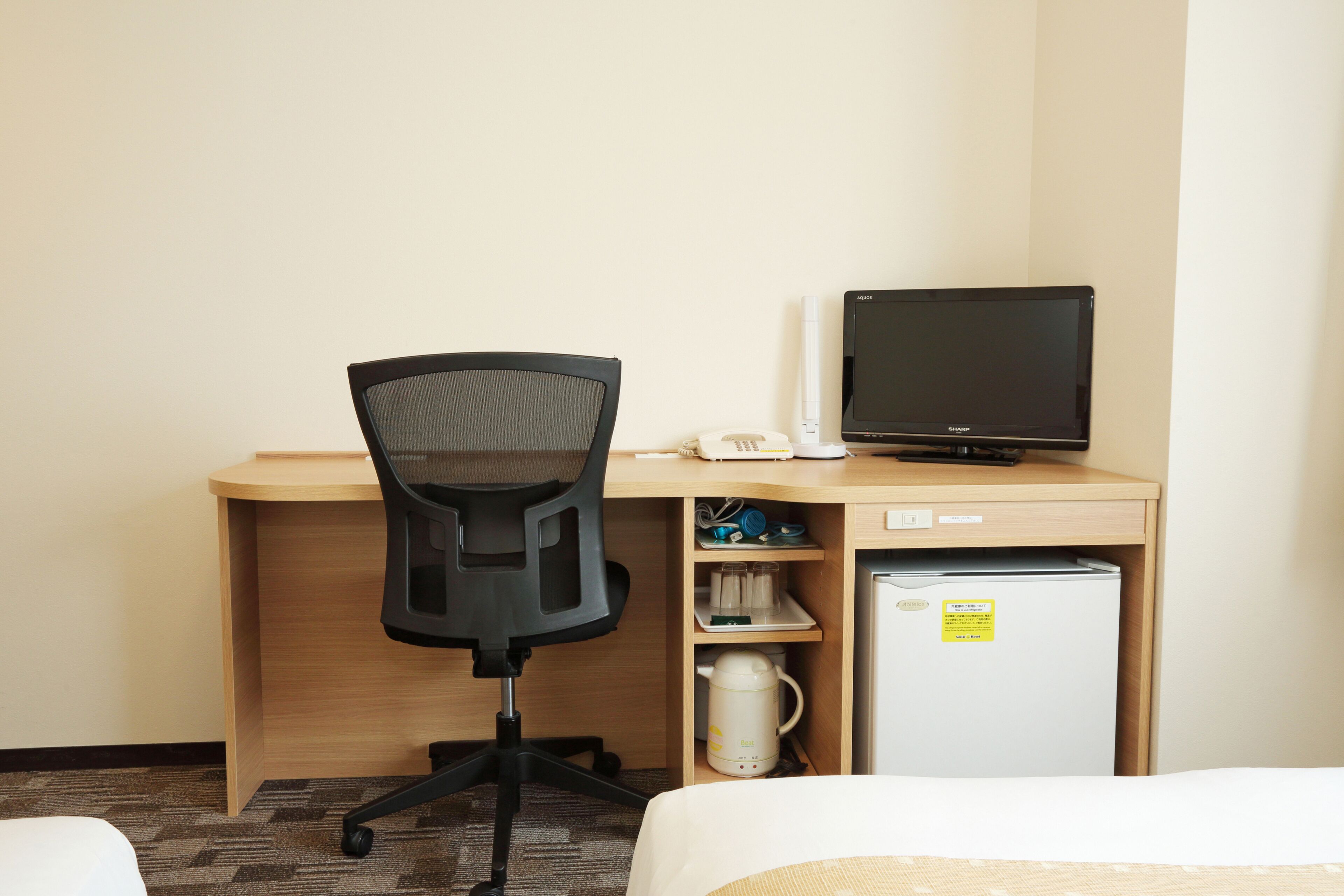 Hotelkamer met een houten bureau, een zwarte bureaustoel, een flatscreen televisie, een minibar en een koffiezetapparaat.