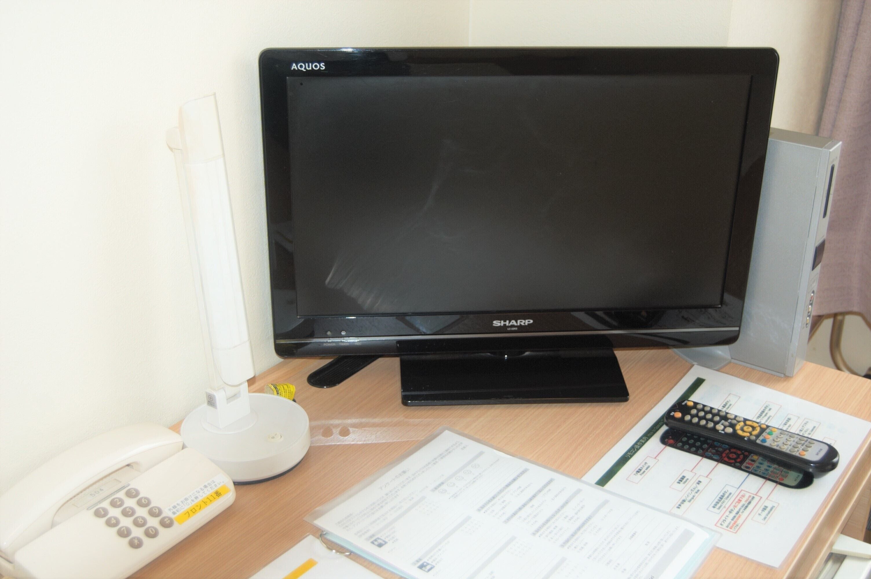 Un téléviseur à écran plat, un téléphone, une télécommande et quelques documents sur un bureau.