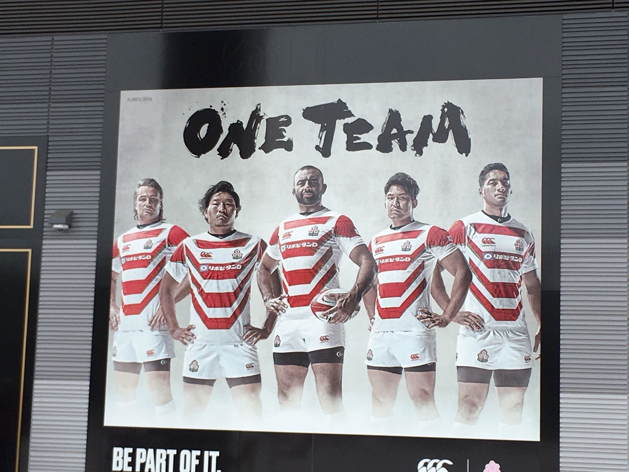 A poster with five rugby players in red and white uniforms, promoting 'ONE TEAM'.