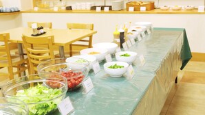 Montaje de bufé con diferentes alimentos en recipientes y una barra de ensaladas con verduras frescas.