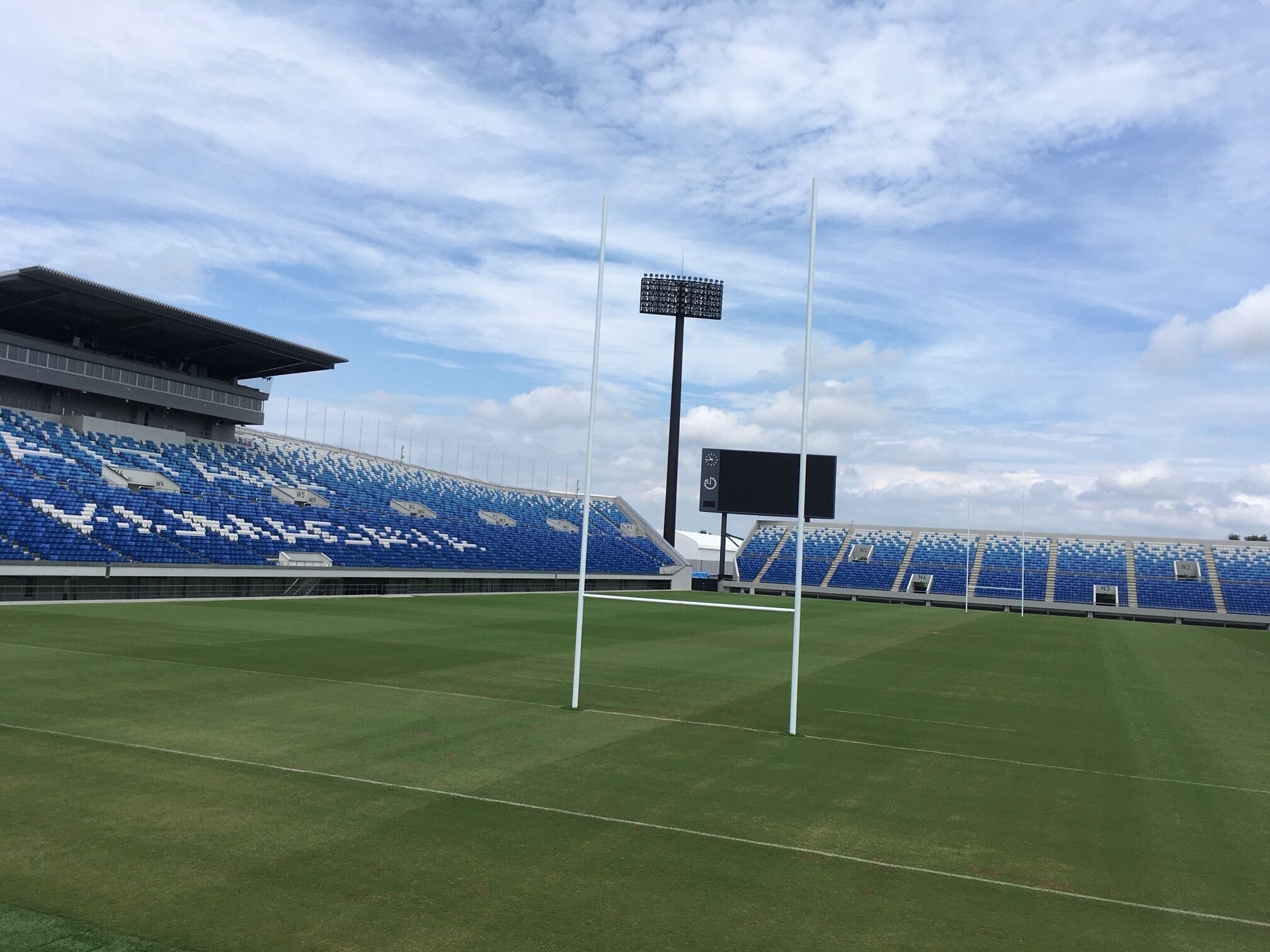A stadium with blue seating, a large scoreboard, and floodlights.
