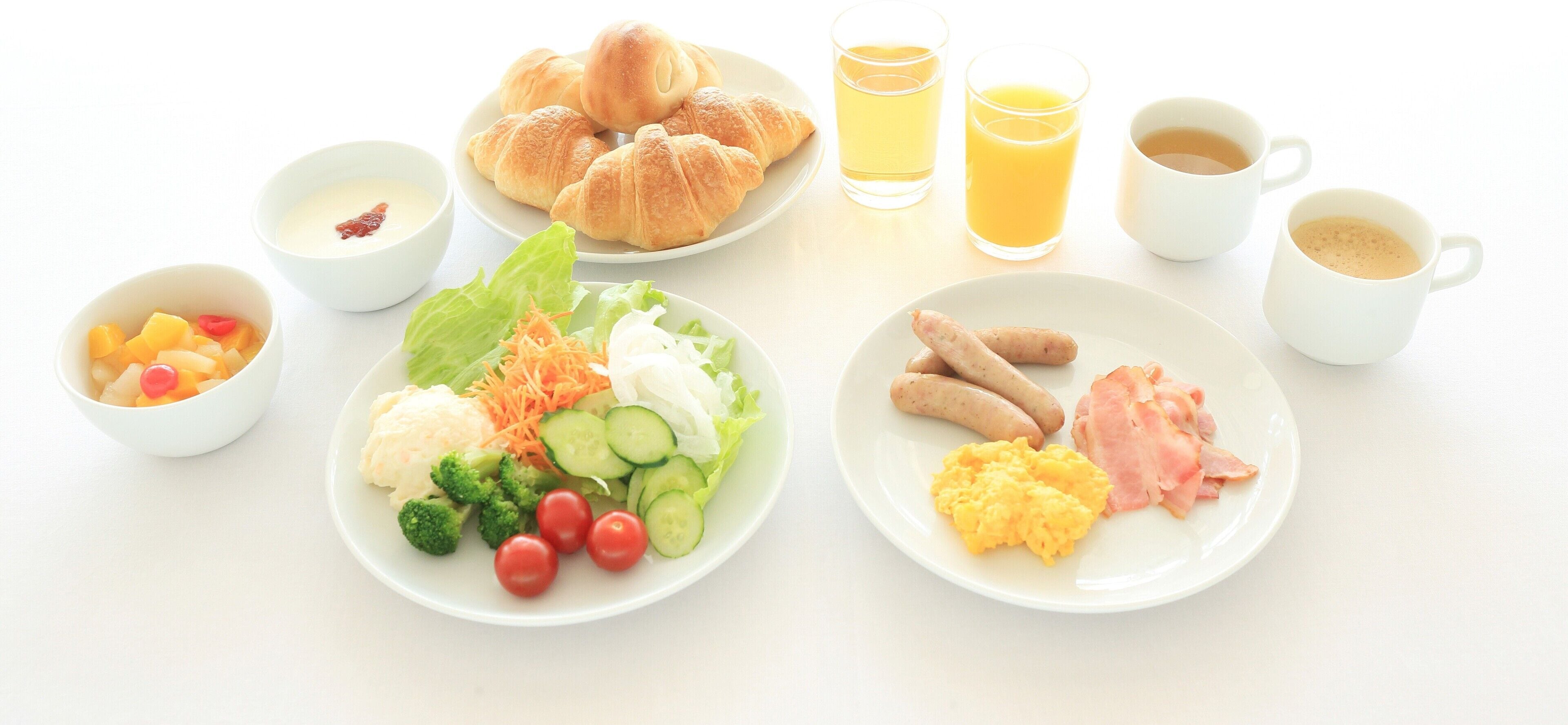 A breakfast table with croissants, fruit, vegetables, scrambled eggs, sausages, and coffee.