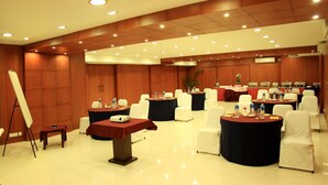 A conference room with round tables, white chairs, and a projector screen. - Shilton Royale (Bengaluru)