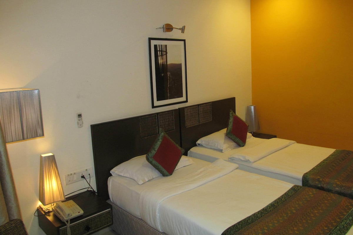 A hotel room with two beds, a bedside lamp, a framed picture on the wall, and a telephone on the nightstand.
