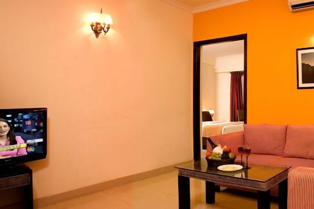 A hotel room with a television, a sofa, a coffee table, and a lamp.