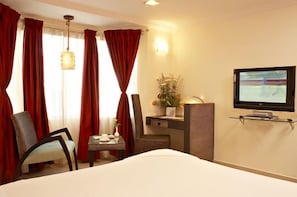A hotel room with a bed, a desk with a lamp, a television, and a chair.