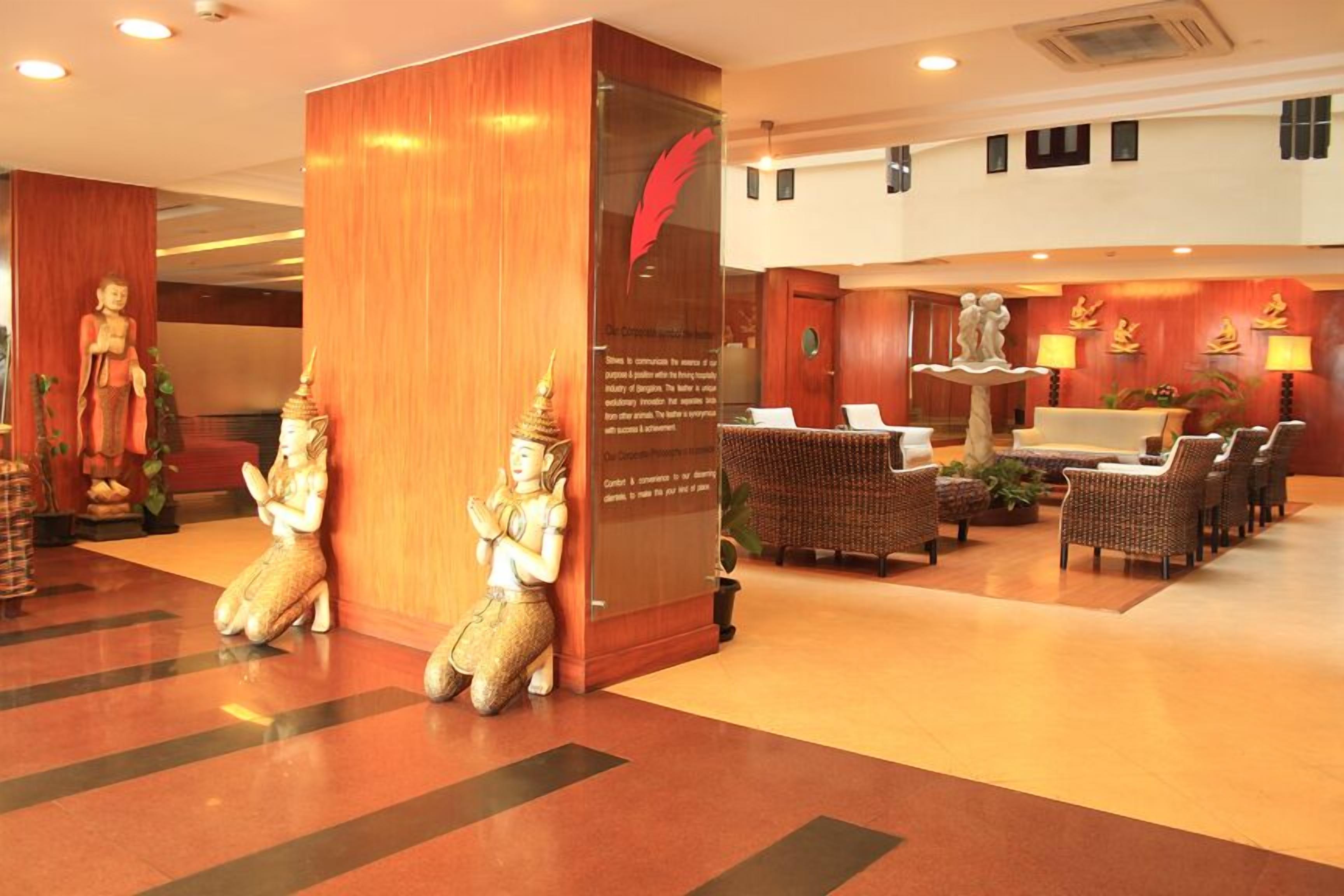 A lobby with a reception desk, wicker chairs, a statue of a deity, and a decorative wall with a red feather.