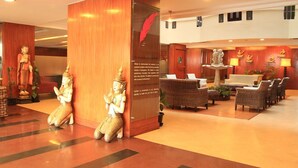A lobby with a reception desk, wicker chairs, a statue of a deity, and a decorative wall with a red feather. - Shilton Royale (Bengaluru)