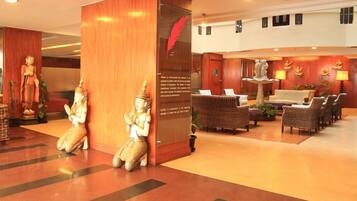 A lobby with a reception desk, wicker chairs, a statue of a deity, and a decorative wall with a red feather.