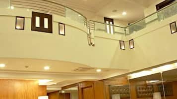 A multi-level hotel lobby with a curved staircase, seating areas, and a large mirror reflecting the space.