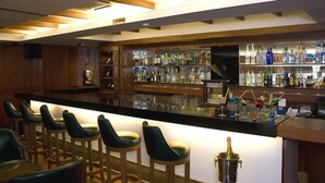 A bar area with wooden bar stools, a counter with a variety of bottles, and a television mounted on the wall. - Shilton Royale (Bengaluru)