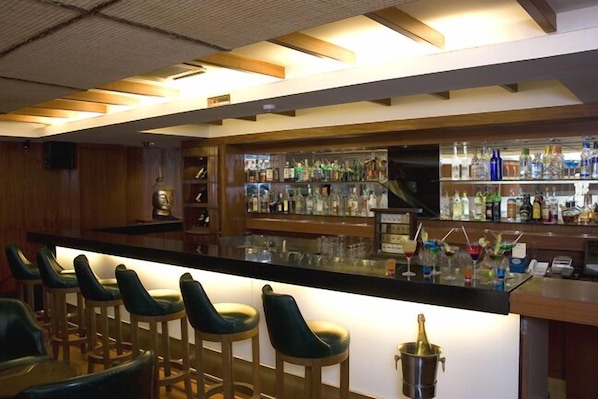 A bar area with wooden bar stools, a counter with a variety of bottles, and a television mounted on the wall.