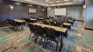 A conference room with multiple tables and chairs, equipped with water bottles, a projector screen, and a presentation screen.