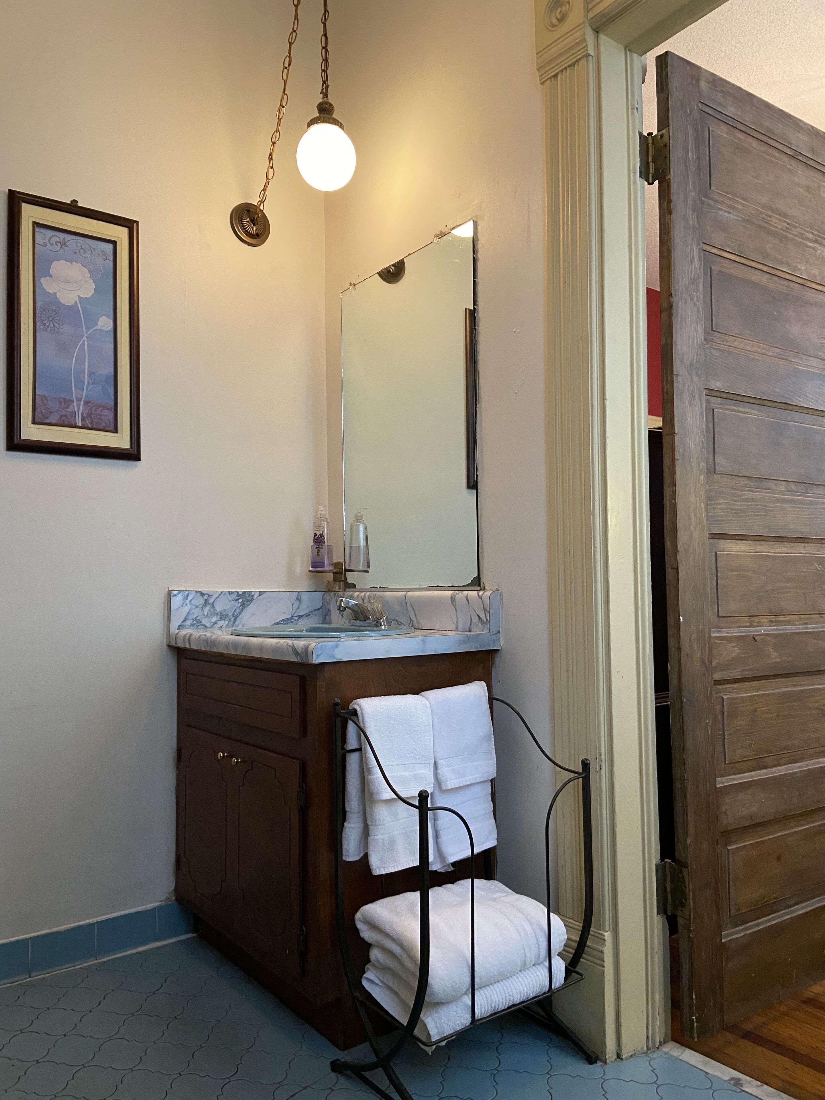 A bathroom with a marble sink, a wooden cabinet, a towel rack with folded towels, a framed picture on the wall, and a wooden door.