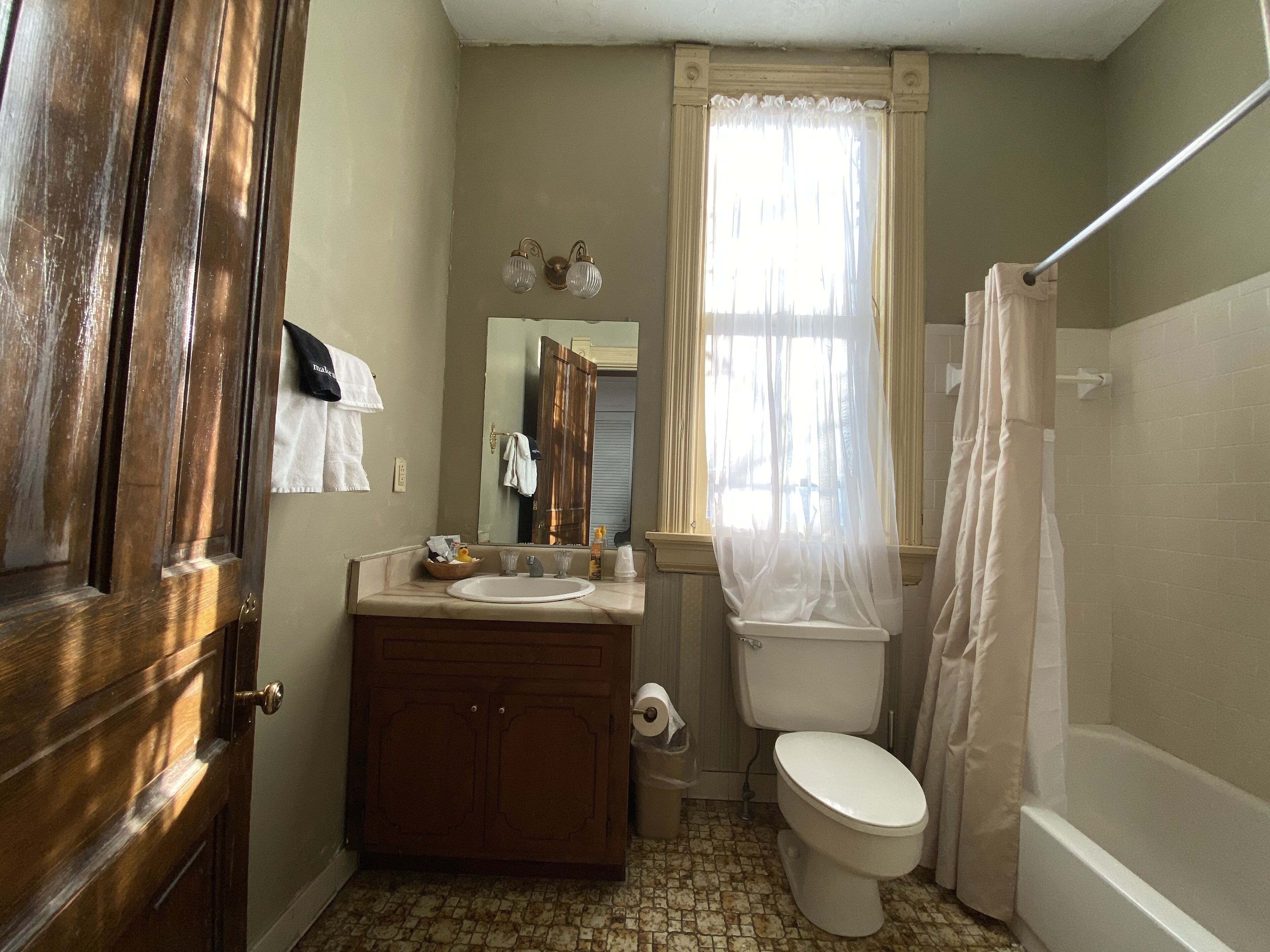 A bathroom with a wooden door, a sink with toiletries, a toilet, and a shower curtain.