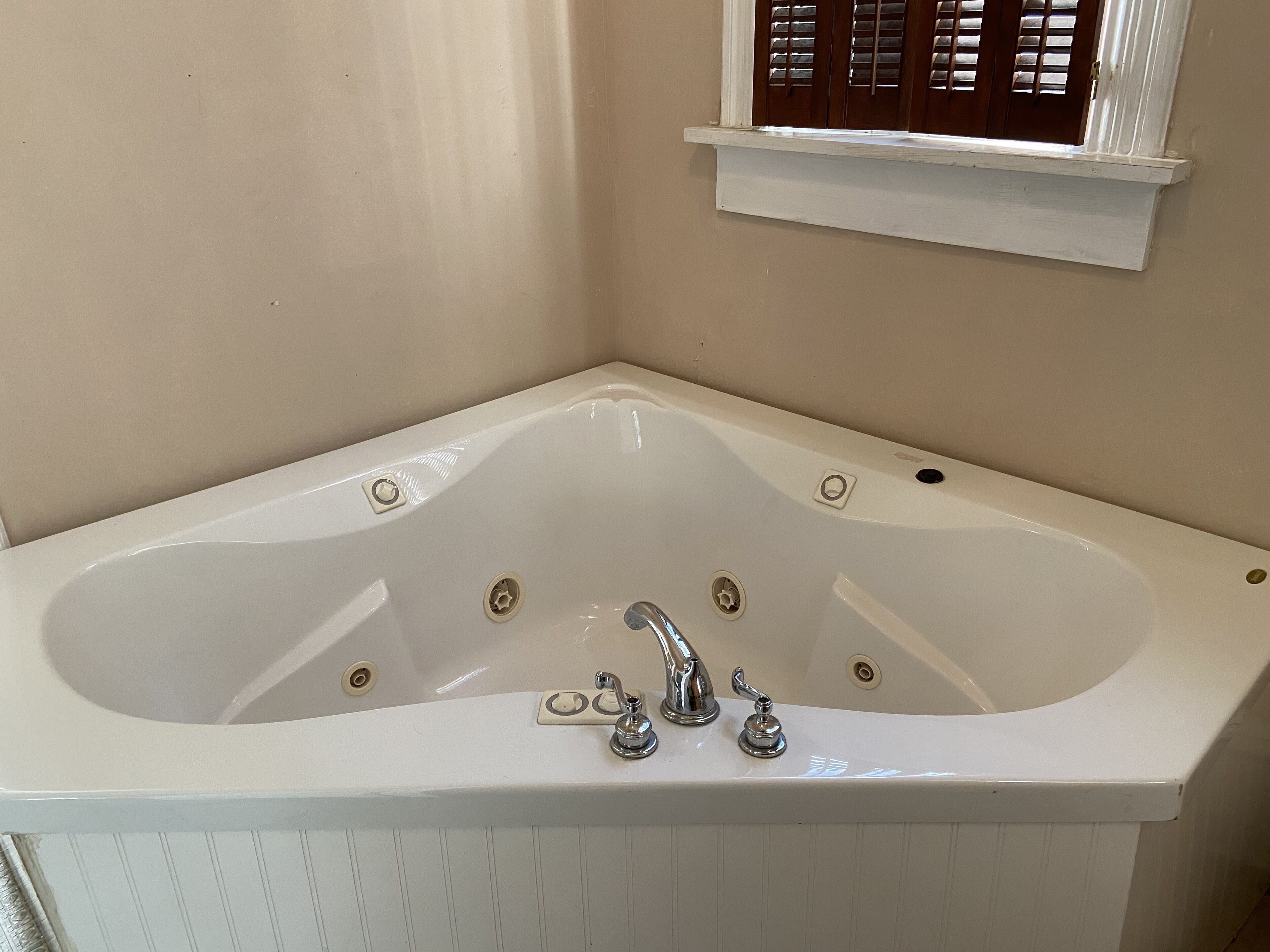 A white freestanding bathtub with two faucets and a window above it.