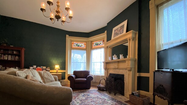 A cozy living room with a fireplace, a large sofa, a patterned rug, and a bookshelf. - The Queen Anne Inn (Augusta)