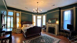 A bedroom with a large bed, a fireplace, a chandelier, and a television. - The Queen Anne Inn (Augusta)