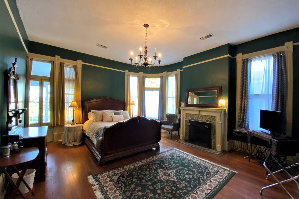 A bedroom with a large bed, a fireplace, a chandelier, and a television.